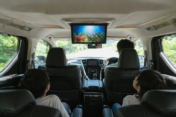 天井から展開されたフリップダウンモニターを後部座席の子どもたちが視聴している右ハンドルのミニバン車内の様子