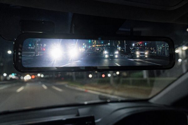 夜間走行時のデジタルインナーミラーの見え方の違い（後続車のヘッドライトが白飛びする状態と、眩しさを抑えて周囲まで見える状態の比較イメージ）